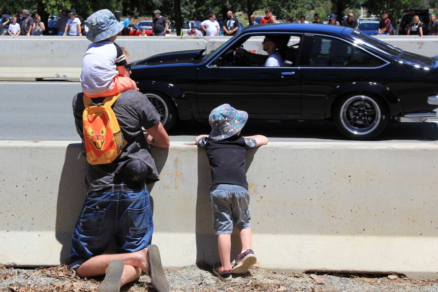 A father and two young sons watch the Summernats city cruise.