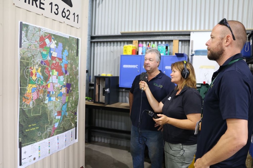 A journalist is interviews eradication team members in front of a colour-coded map depicting 60 cane farms in the target area