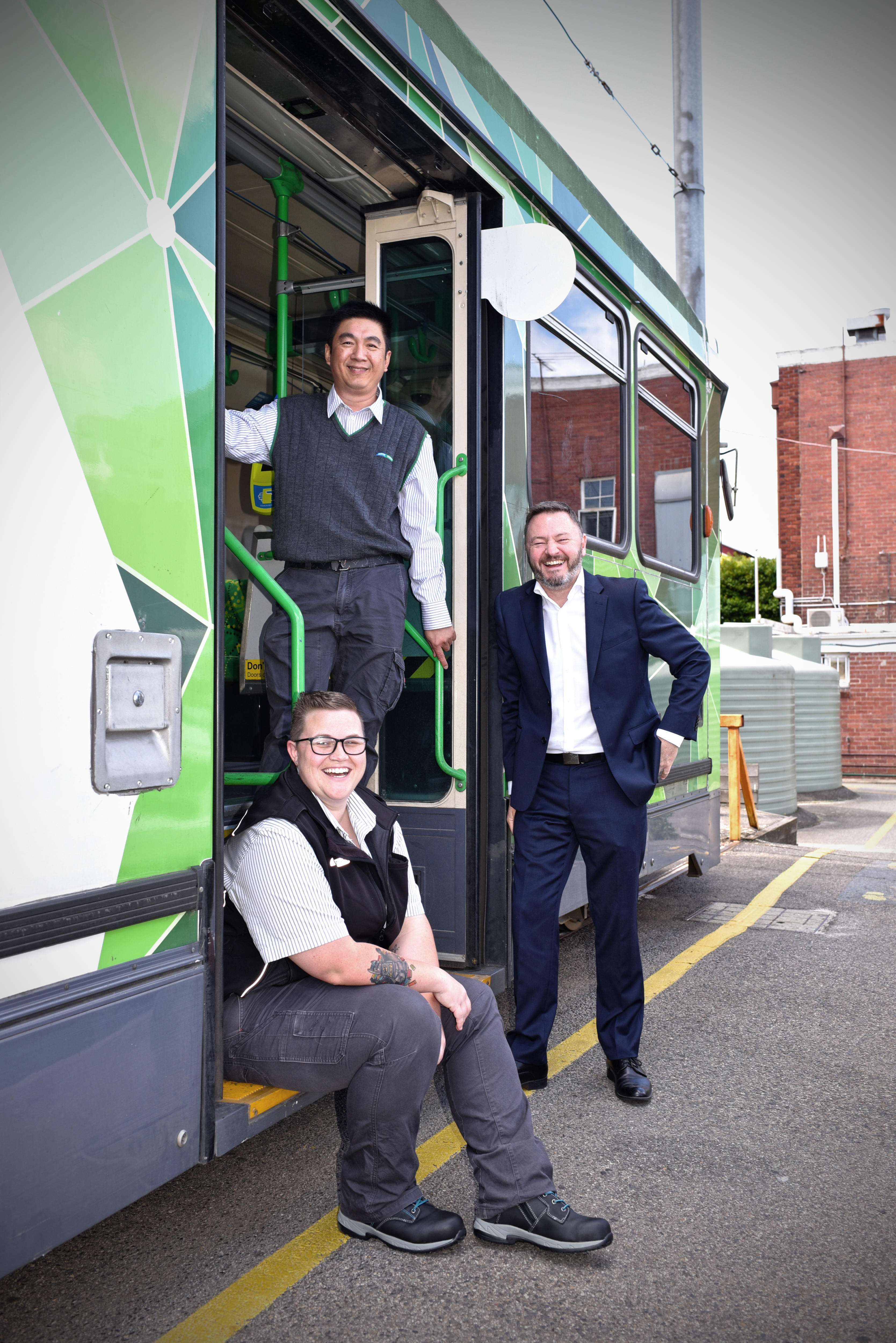 Three people smiling at the camera at an opening of a tram