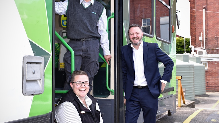 Three people smiling at the camera at an opening of a tram