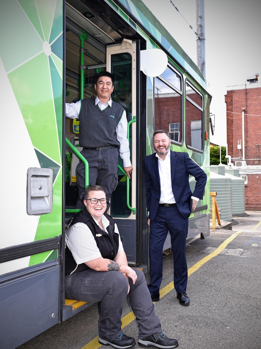 Three people smiling at the camera at an opening of a tram