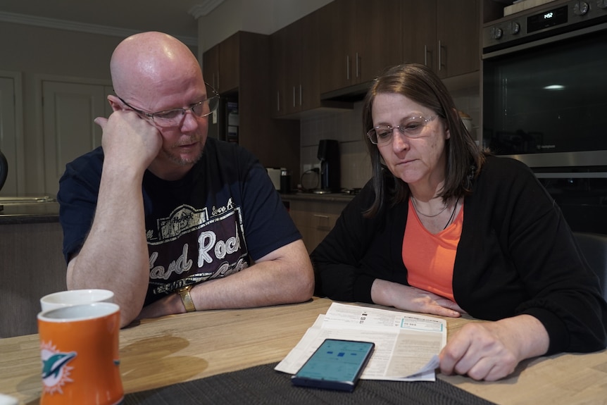 Wayne and Sam sitting at a wooden table and reading through bills.