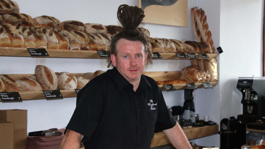 Perth baker Andrew Ritchie standing behind the counter of his bakery with bread stacked on shelves behind him