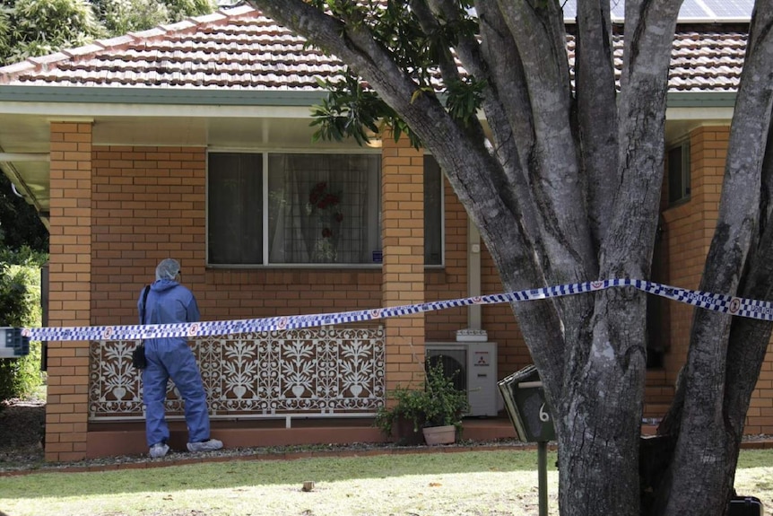 A forensic investigator at a house with police tape across the front yard.