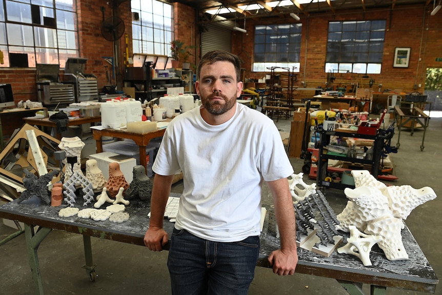 a man leans on a table of small sculptures in a studio 
