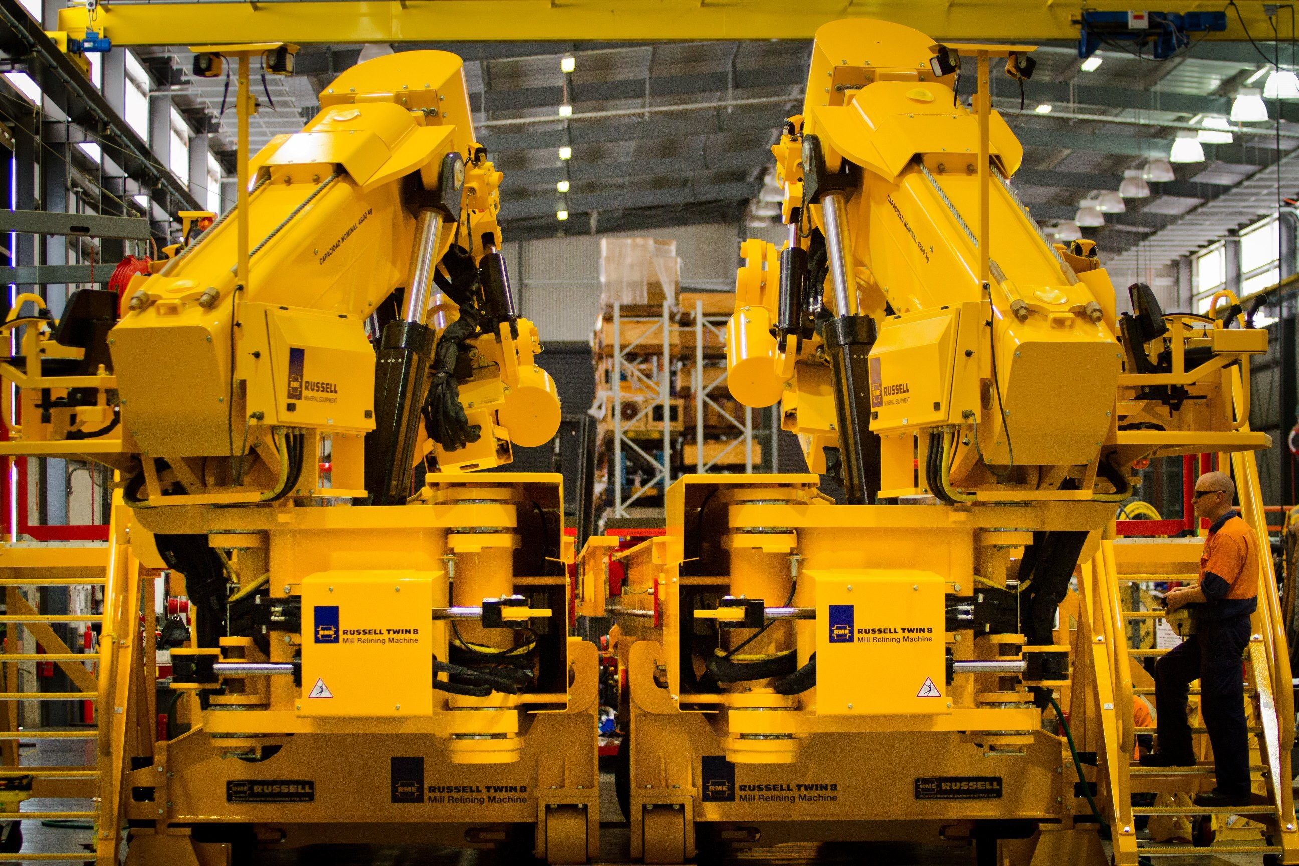 A man looks tiny standing on the side of a large piece of mining machinery. It's brightly coloured, with pistons and equipment
