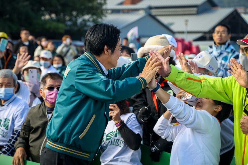 Lai Ching-te wears a green varsity jacket, high-fiving people in a crowd