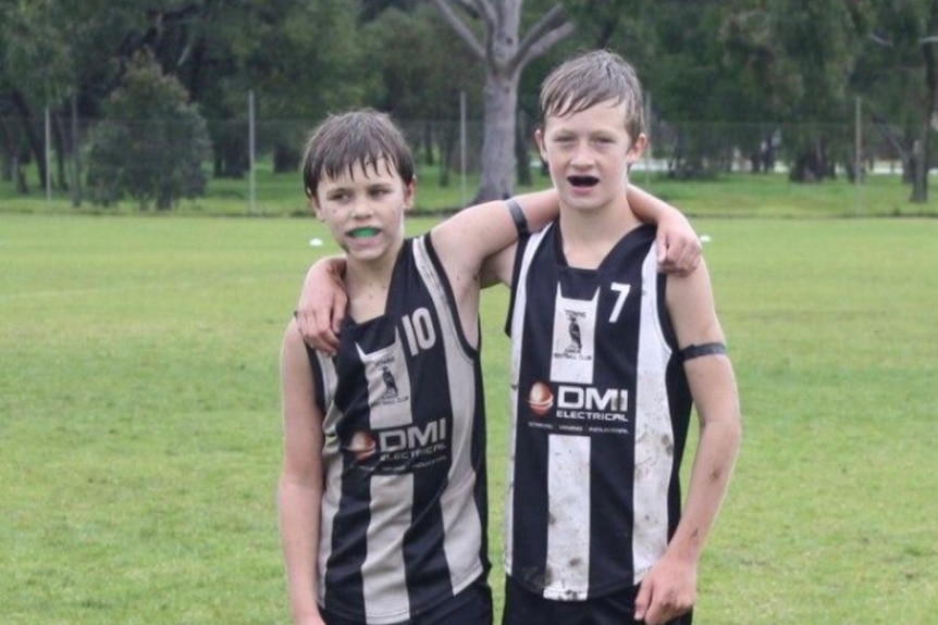 Two young boys with their arm around each other dressed in black and white striped footy clothes.