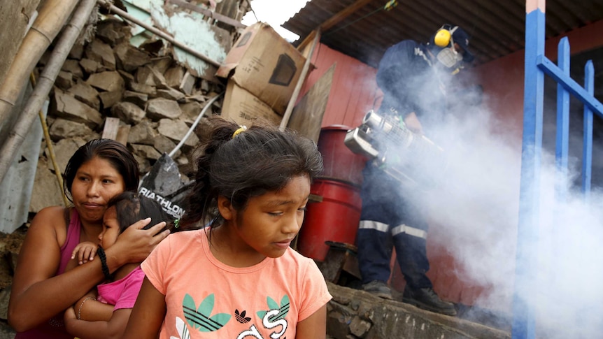 A health worker fumigates a house as residents wait outside during a campaign against the Zika virus.