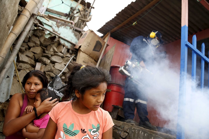 A health worker fumigates a house as residents wait outside during a campaign against the Zika virus.