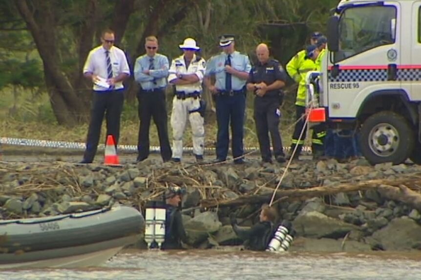 A group of emergency service workers stand above the Tweed River as police divers swim below them