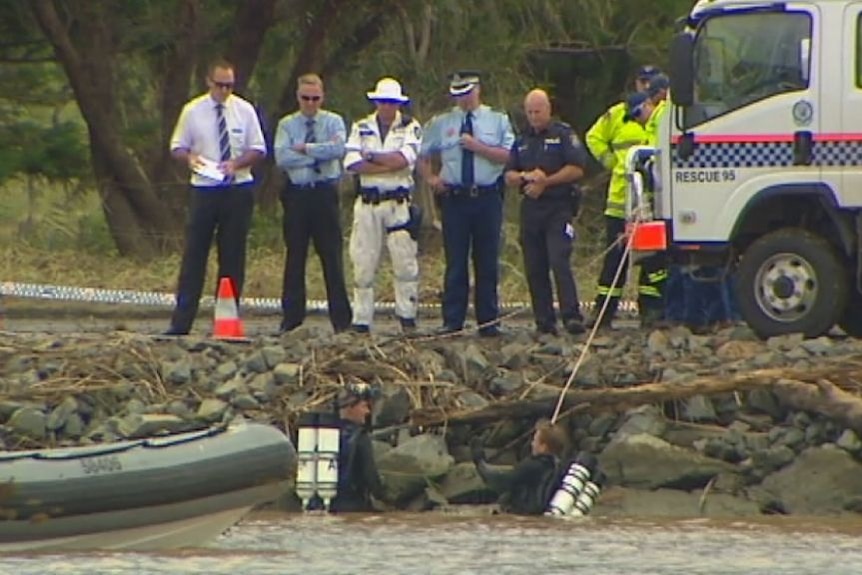 A group of emergency service workers stand above the Tweed River as police divers swim below them