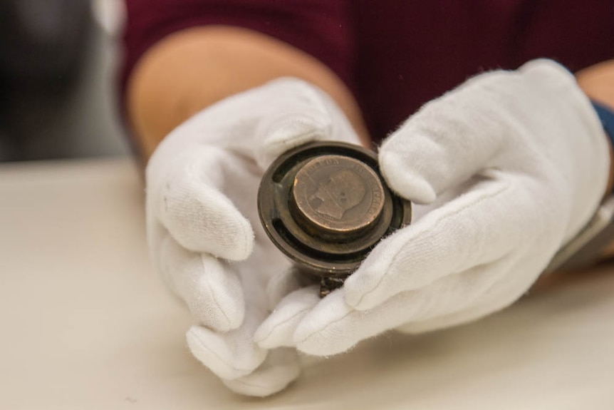 Hands hold a 1856 Napoleon coin fixed to the lid of an inkwell.