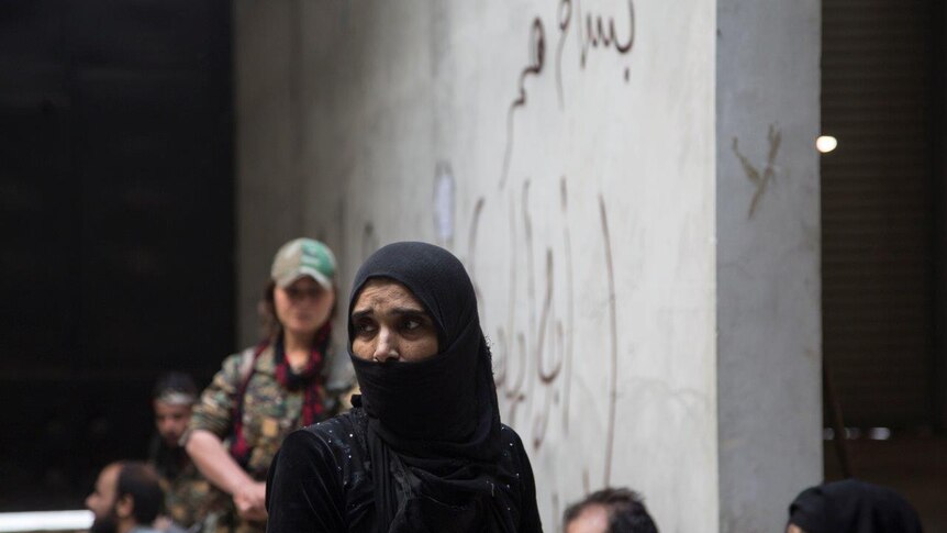 A YPJ fighter ( back) stands guard close to suspected Daesh family members