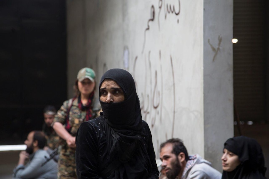 A YPJ fighter ( back) stands guard close to suspected Daesh family members