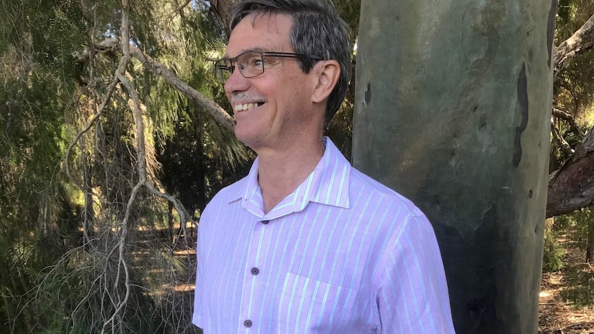 A mid-shot of Mike Nahan smiling and standing in front of a tree.