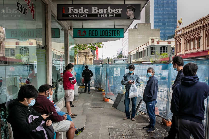 A goup of men standing and sitting outside a barber's shop. 