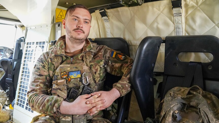 A man with a small moustache and dressed in camo sits inside a military vehicle
