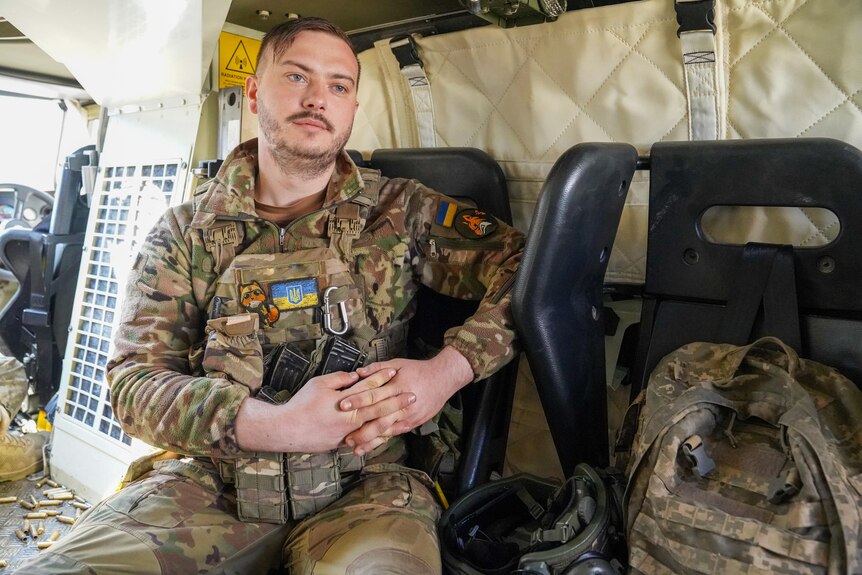 A man with a small moustache and dressed in camo sits inside a military vehicle