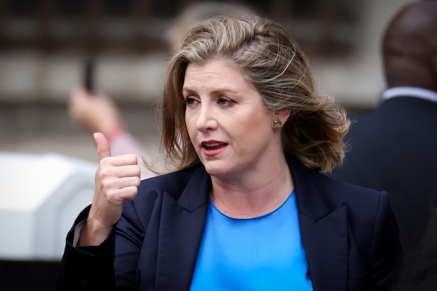 A woman in a blue blazer gives a thumbs up