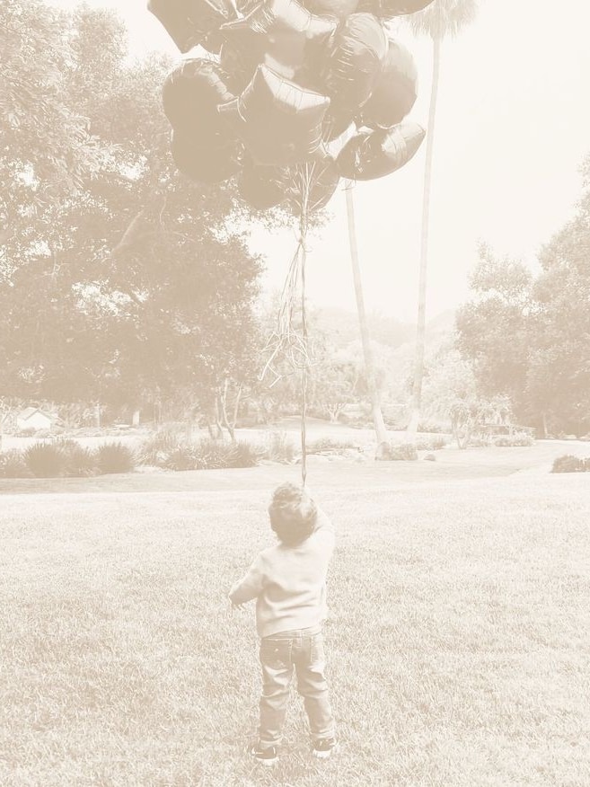 A sepia photo of a young boy holding balloons.