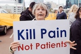 A woman holds up a white sign reading 'Kill Pain Not Patients'.