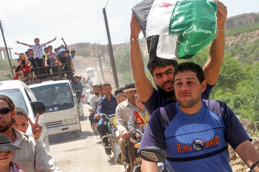 Opposition fighters and supporters ride through the streets on motorbikes and tray trucks displaying opposition flags.