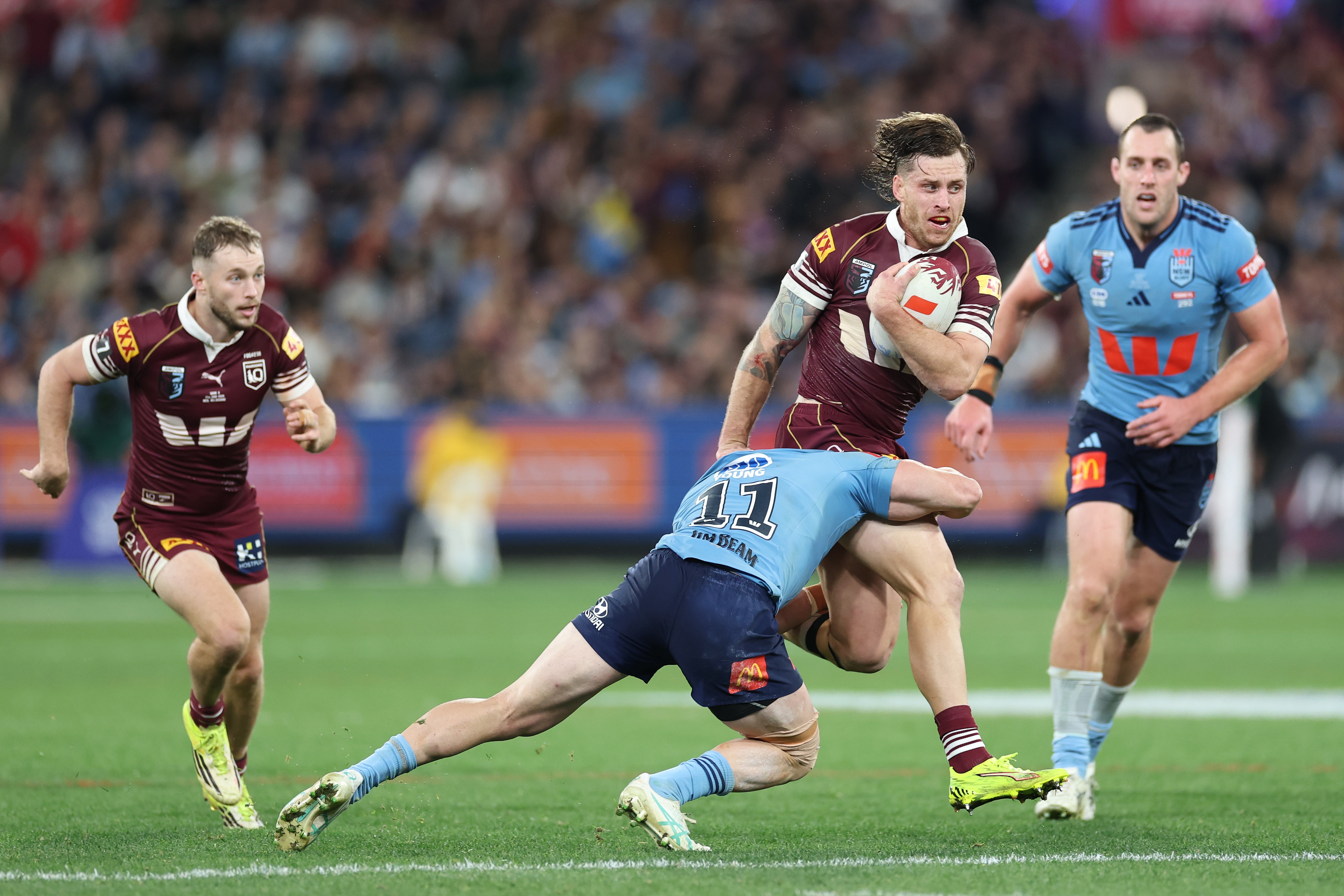 Sam Walker runs on pitch behind his teammate who has the ball as he gets tackled by an opponent.