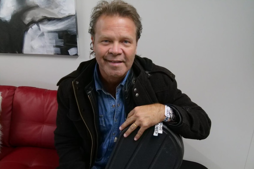 A man in a black jacket and blue shirt looks at the camera