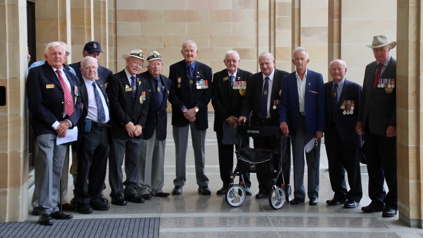 A group of ex-servicemen wearing their service medals, stand in a line outside WA's Parliament.