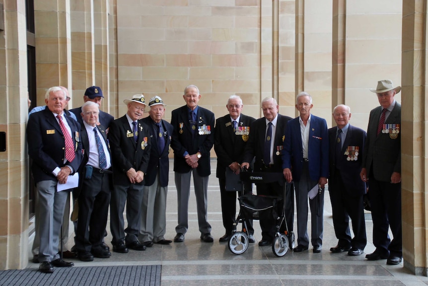 A group of ex-servicemen wearing their service medals, stand in a line outside WA's Parliament.