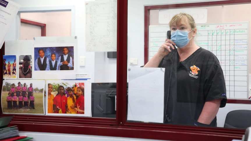 A health worker stands and talks on the phone, looking at a roster.