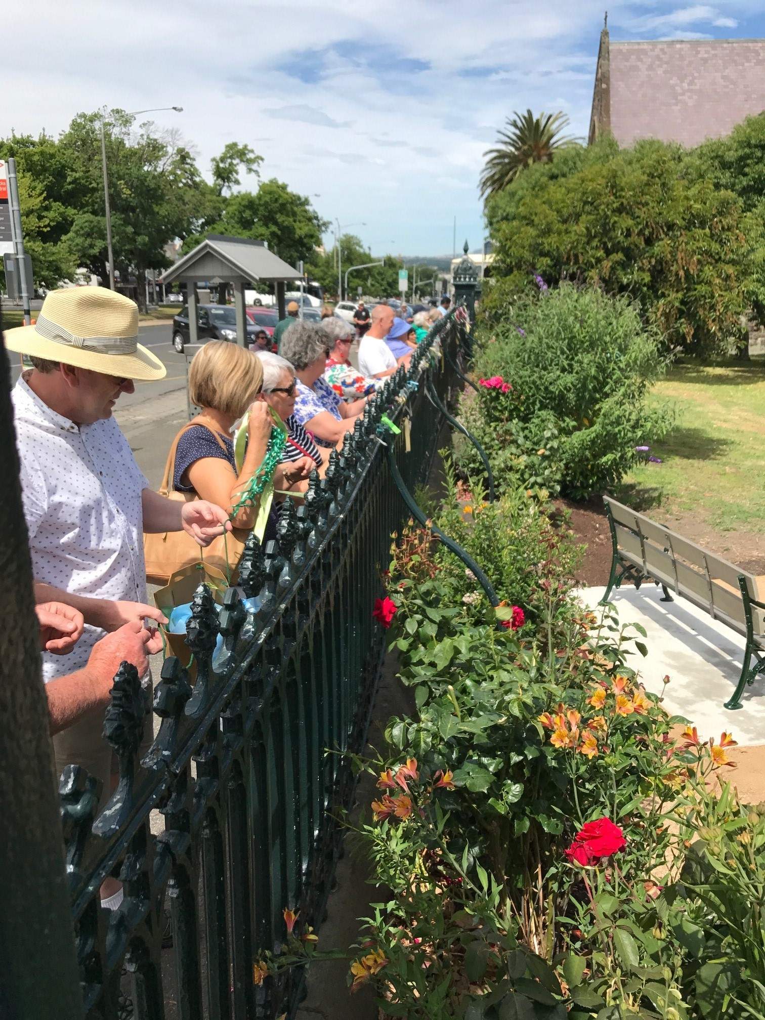 A line of people cut ribbons from the fence St. Patrick's Catholic Cathedral in Ballarat on a sunny day.