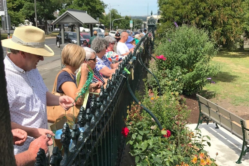 A line of people cut ribbons from the fence St. Patrick's Catholic Cathedral in Ballarat on a sunny day.