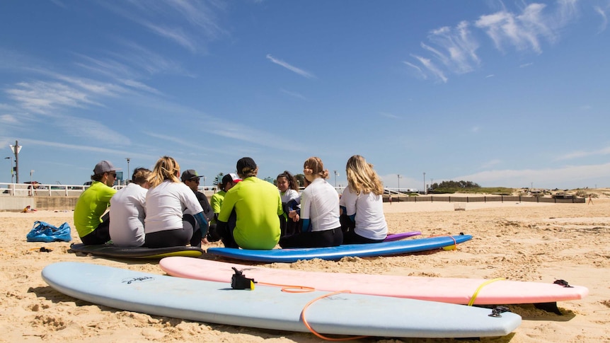 Surfboards lie on a beach while people speak in the background.