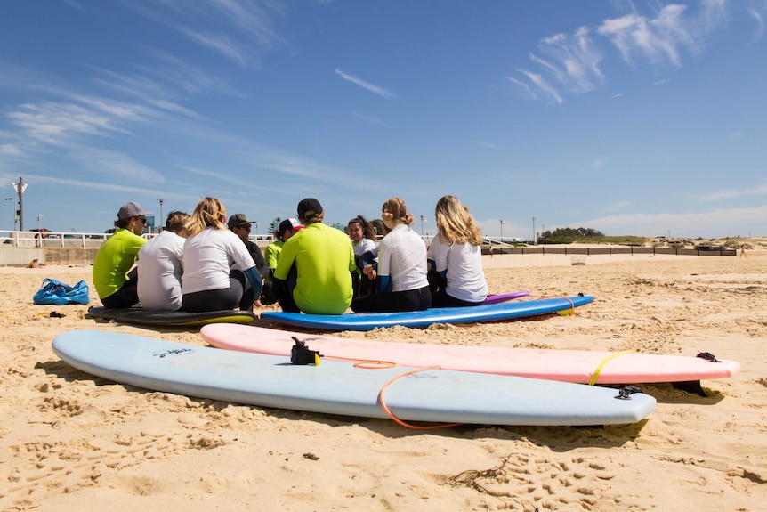 Surfboards lie on a beach while people speak in the background.