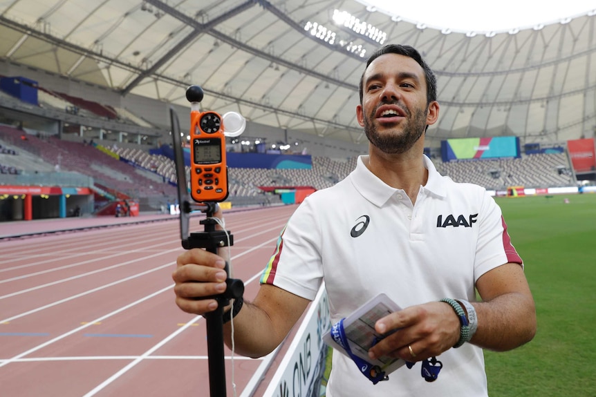 A researcher stands on the side of an athletics track holding a sensor on a stand.