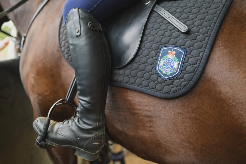 A police officers boot sits in a steerup of a saddle.