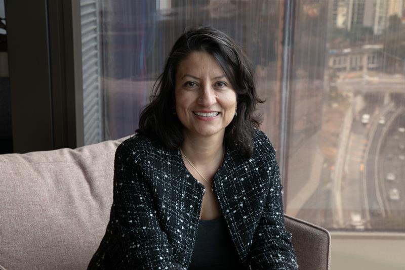 Uma mulher com uma jaqueta preta estilo tweed sentada em um sofá.