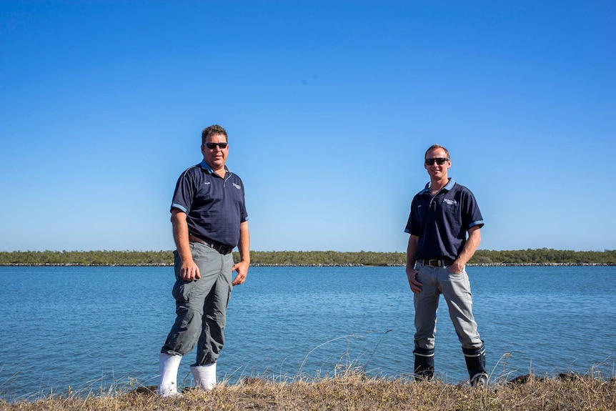 Two men stand on river bank.