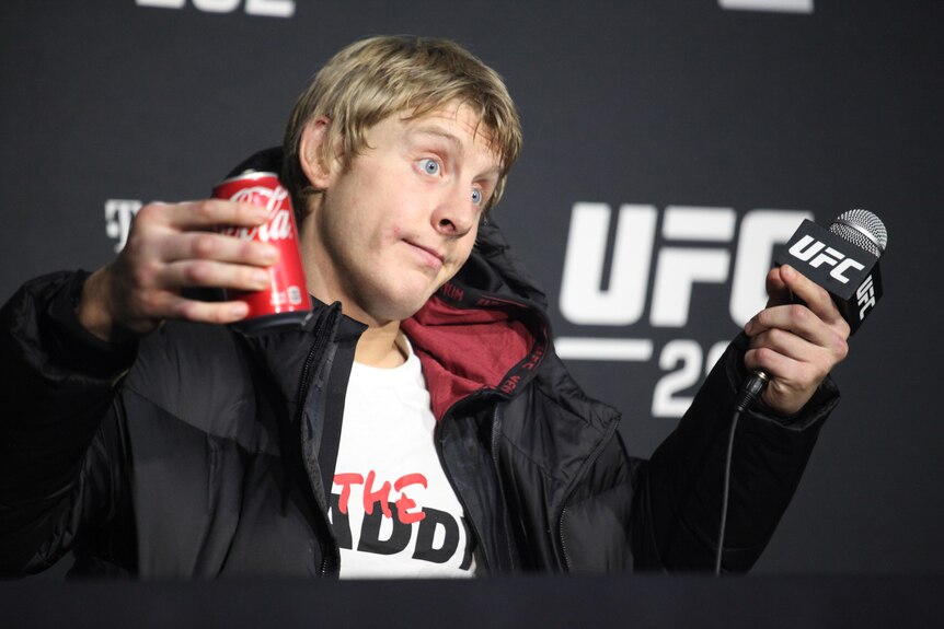 Paddy Pimblett shrugs while holding a can of coke and a microphone at a UFC press conference.