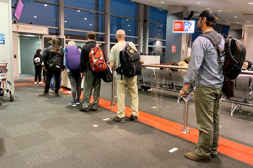 A group of Qantas passengers with backpacks stand in a queue ready to board a plane.