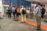 A group of Qantas passengers with backpacks stand in a queue ready to board a plane.