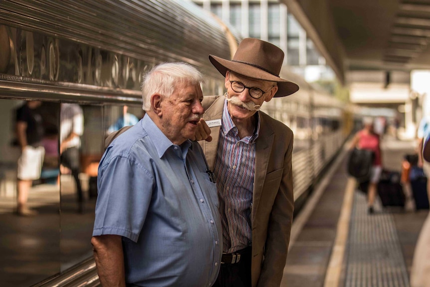 Two men about to board a train at a railway platform.