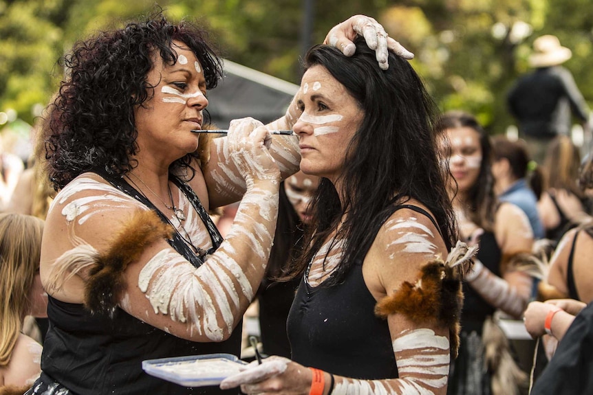 Colour photo of Ceane Towers of Wagana Dancers applying group leader Jo Clancy with ochre backstage at Dance Rites 2018.