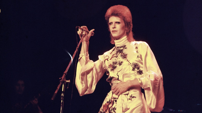 david bowie in a very short silk robe on stage in ziggy stardust makeup and red hair