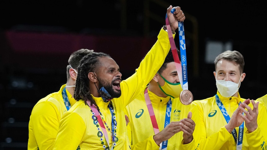 Patty Mills holds his bronze medal in the air at the Tokyo Olympics men's basketball medal ceremony.