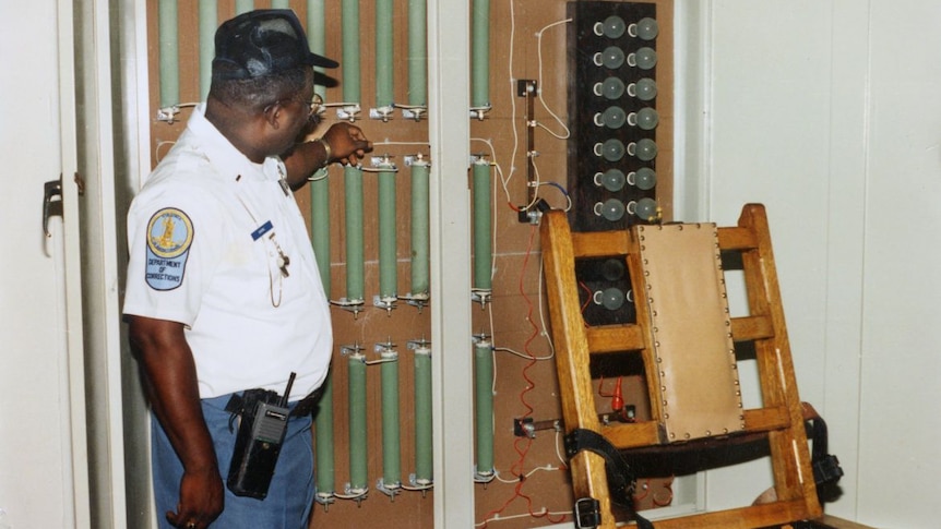 A man in a uniform standing next to an electric chair