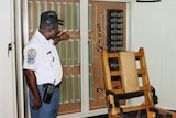A man in a uniform standing next to an electric chair