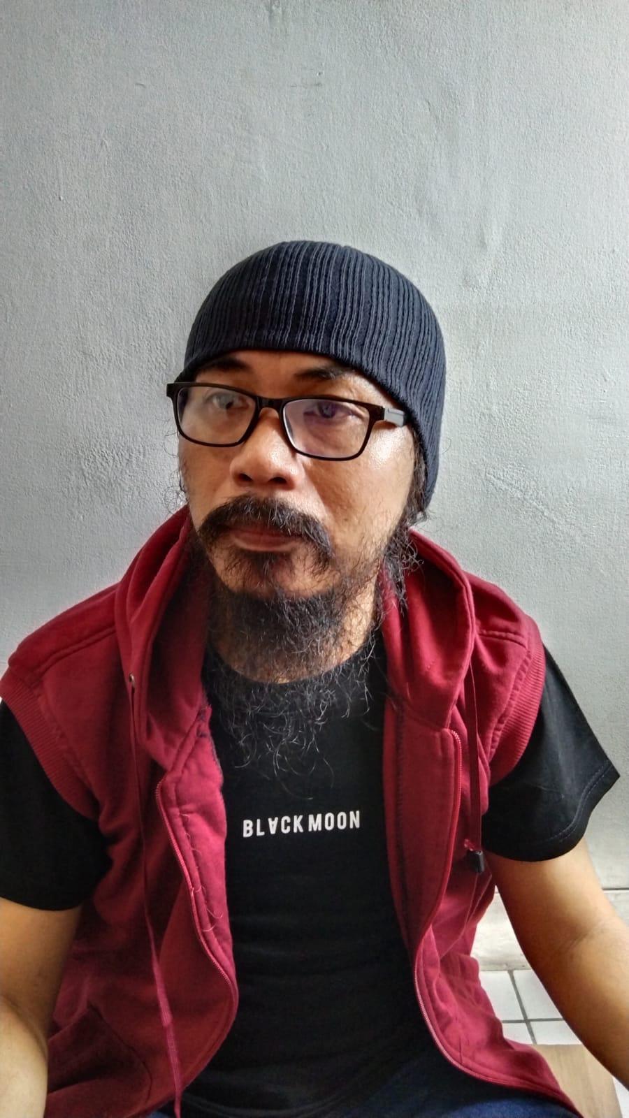 Man with glasses, black hat, beard and mustache looking at the camera.